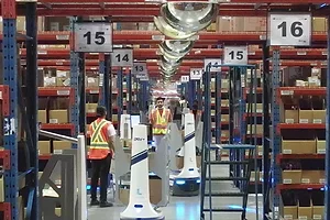WORKERS IN A WAREHOUSE MINGLE WITH ROBOTS IN NUMBERS AISLES