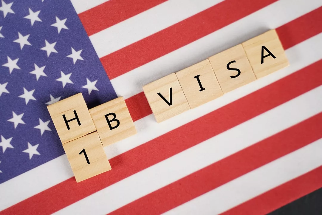 "h-1b visa" spelled out in wooden tiles on top of an American flag
