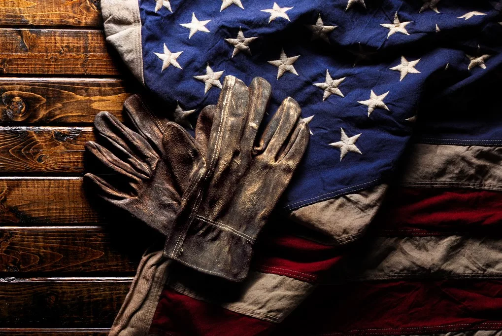 A PAIR OF WELL-WORN WORK GLOVES SIT ATOP AN AMERICAN FLAG