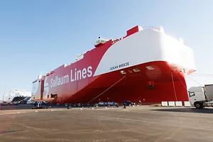 A red and white container vessel docked at a port, that reads "Sallaum Lines" in white writing along the side.