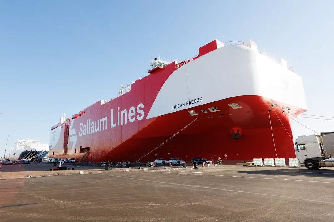 A red and white container vessel docked at a port, that reads "Sallaum Lines" in white writing along the side.