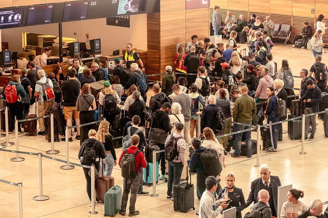 PASSENGERS PULLING SUITCASES MILL AROUND, SOME FORMING LINES, AT AN AIRPORT TERMINAL