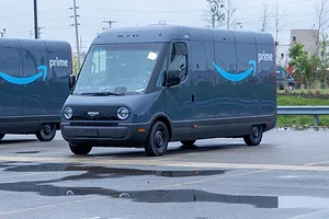 TWO BLUE DELIVERY VANS BEARING THE AMAZON LOGO SIT IN A WET PARKING LOT