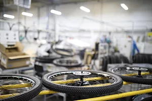 A row of three detached bicycle wheels sitting on a row of three yellow bars in a warehouse