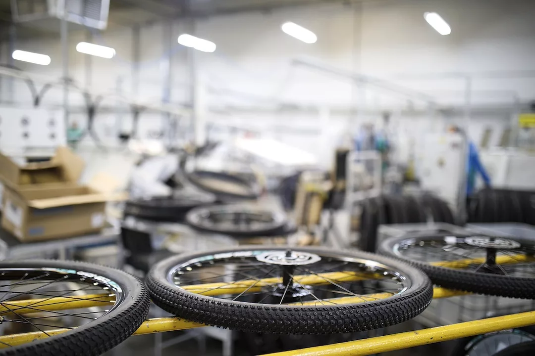 A row of three detached bicycle wheels sitting on a row of three yellow bars in a warehouse