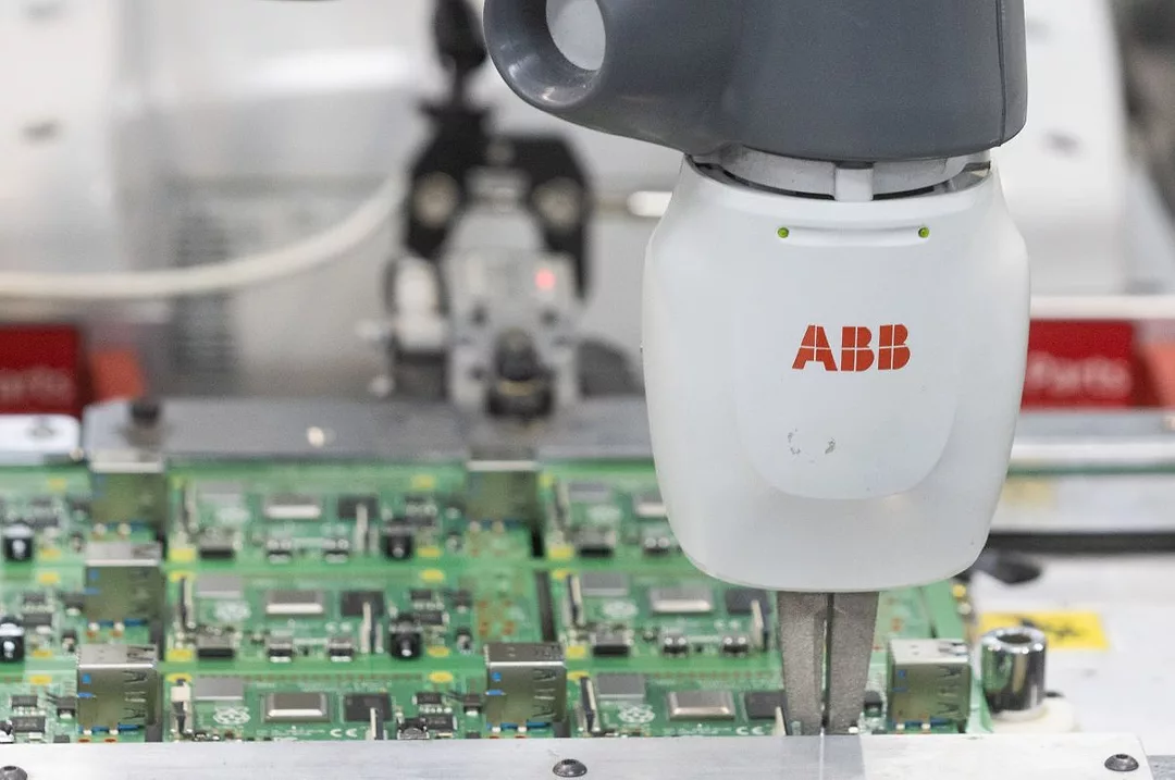 A ROBOTIC TOOL BEARING THE ABB LOGO WORKS ON A CIRCUIT BOARD