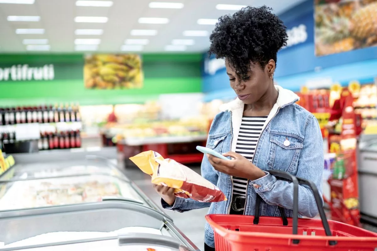 A SHOPPER USES A SMARTPHONE TO SCAN A LABEL ON AN ITEM IN A GROCERY STORE AISLE