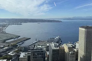 A large blue body of water surrounded by a city coastline dotted with skyscrapers, with a mountain range along the horizon