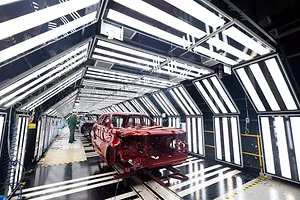 A PARTIALLY BUILT CAR SITS IN A TUNNEL OF LIGHTS, ATTENDED BY A WORKER