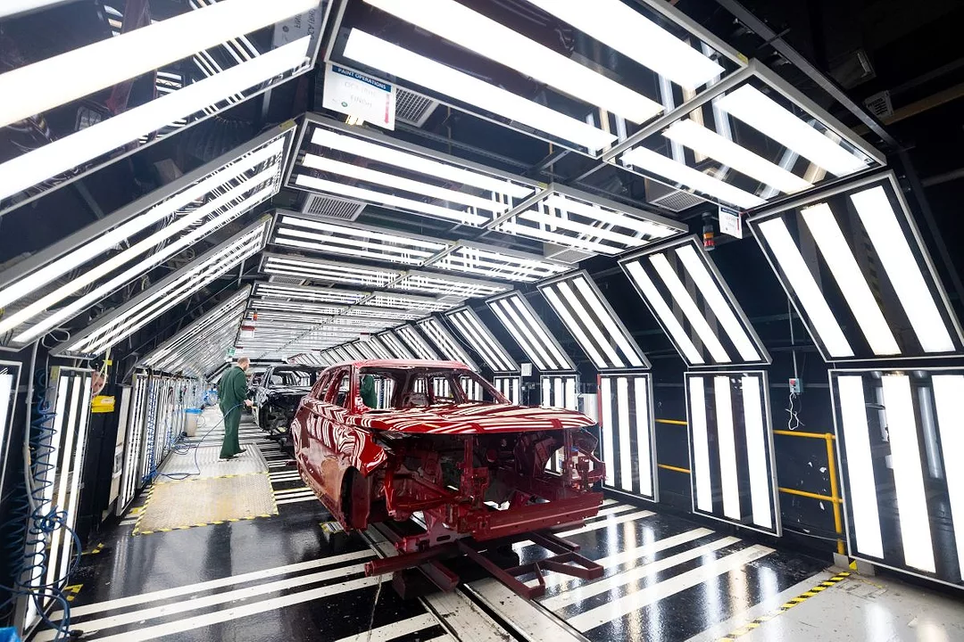 A PARTIALLY BUILT CAR SITS IN A TUNNEL OF LIGHTS, ATTENDED BY A WORKER