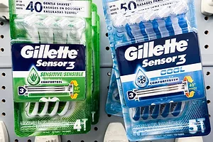 BRIGHT GREEN AND BLUE PACKETS OF GILLETTE DISPOSABLE RAZORS SIT ON A STORE SHELF.