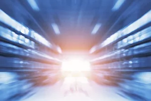 A BLURRED IMAGE OF WAREHOUSE RACKING WITH A ROBOT'S HEADLIGHT IN THE MIDDLE OF THE AISLE