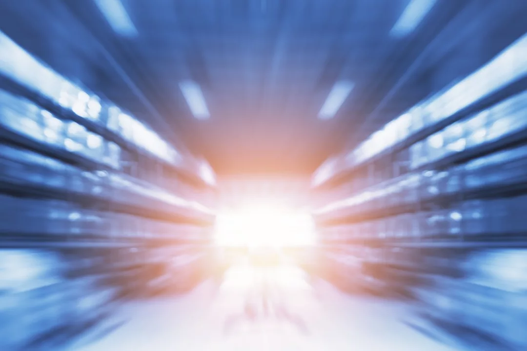 A BLURRED IMAGE OF WAREHOUSE RACKING WITH A ROBOT'S HEADLIGHT IN THE MIDDLE OF THE AISLE