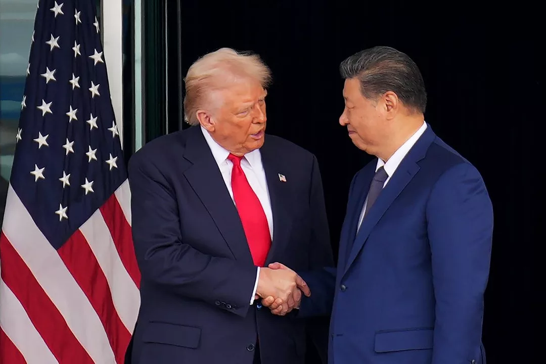 TWO MEN IN BLUE SUITS SHAKE HANDS IN FRONT OF AN AMERICAN FLAG