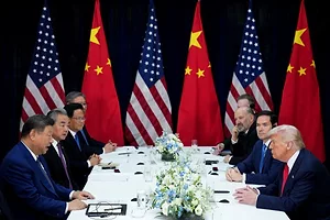 A GROUP OF MEN IN SUITS SIT AROUND A TABLE, FRAMED BY CHINESE AND AMERICAN FLAGS