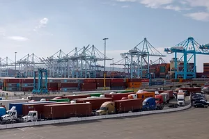 VIEW OF A BUSY PORT, WITH CRANES IN THE BACKGROUND AND LINES OF TRUCKS IN THE FOREGROUND