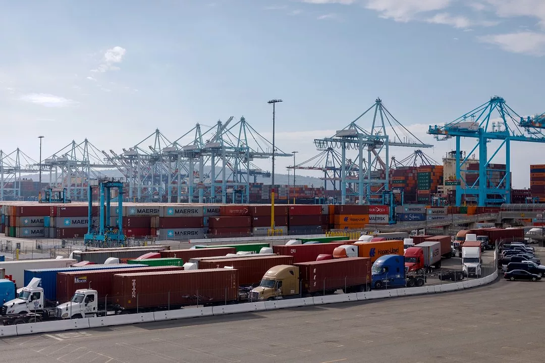 VIEW OF A BUSY PORT, WITH CRANES IN THE BACKGROUND AND LINES OF TRUCKS IN THE FOREGROUND