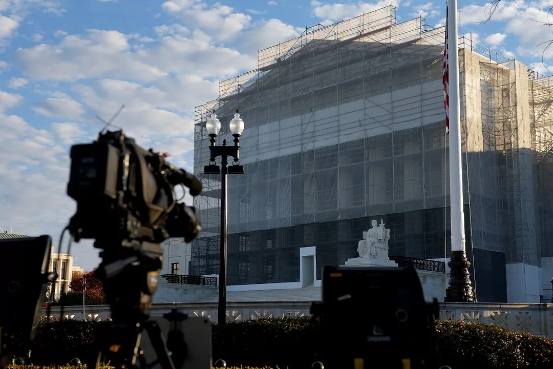 A CAMERA CREW SETS UP OUTSIDE A BUILDING