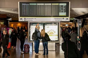 Travelers look at an arrivals and departures board at a busy airport.