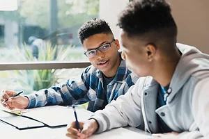 TWO YOUNG STUDENTS DISCUSS MATTERS OVER A DESK