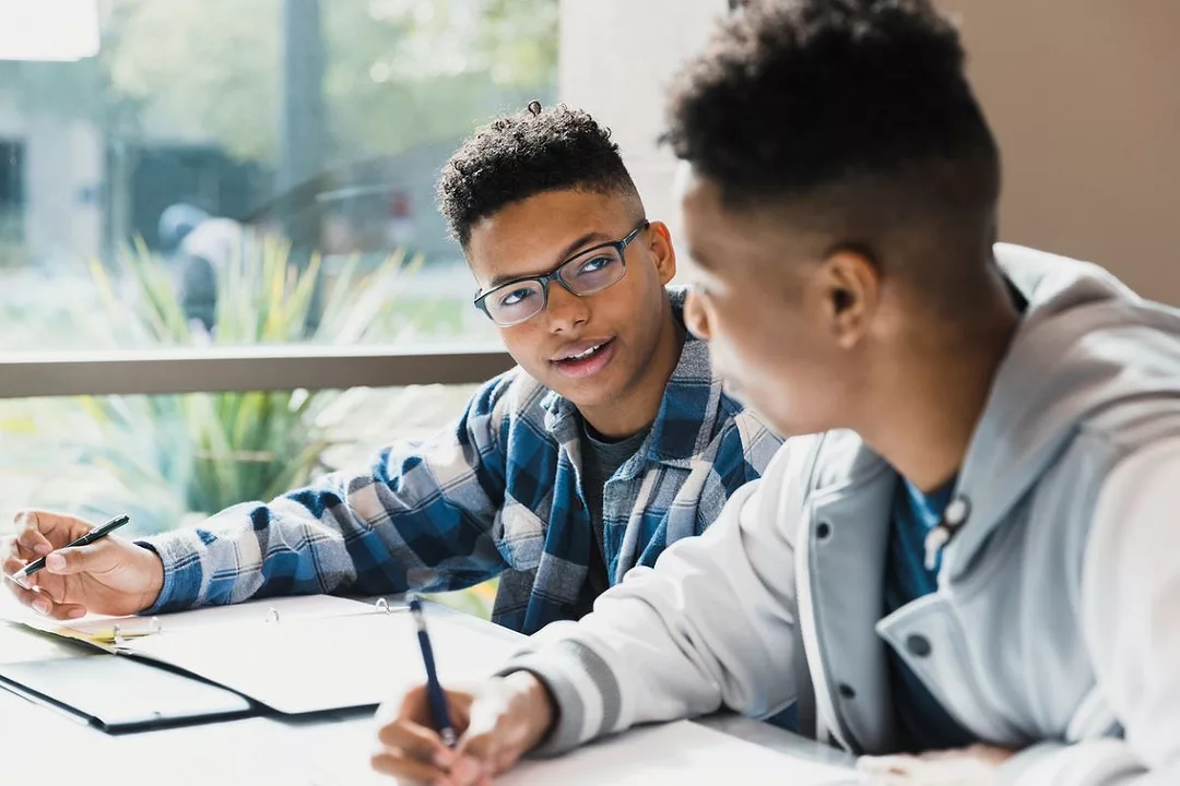 TWO YOUNG STUDENTS DISCUSS MATTERS OVER A DESK