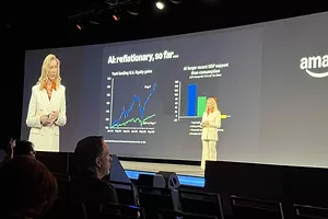 A blonde woman in a white suit standing on a stage, with a graph behind her on a large screen