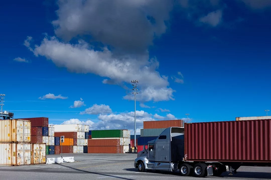 A LOADED TRUCK APPROACHES A DOCK FULL OF CONTAINERS