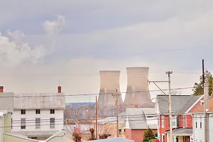 Two white concrete nuclear smokestacks, towering above a modest town dotted with white and red brick homes in the foreground