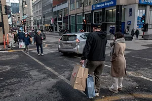 SHOPPERS CROSS A BUSY STREET IN A CITY, CARRYING SHOPPING BAGS