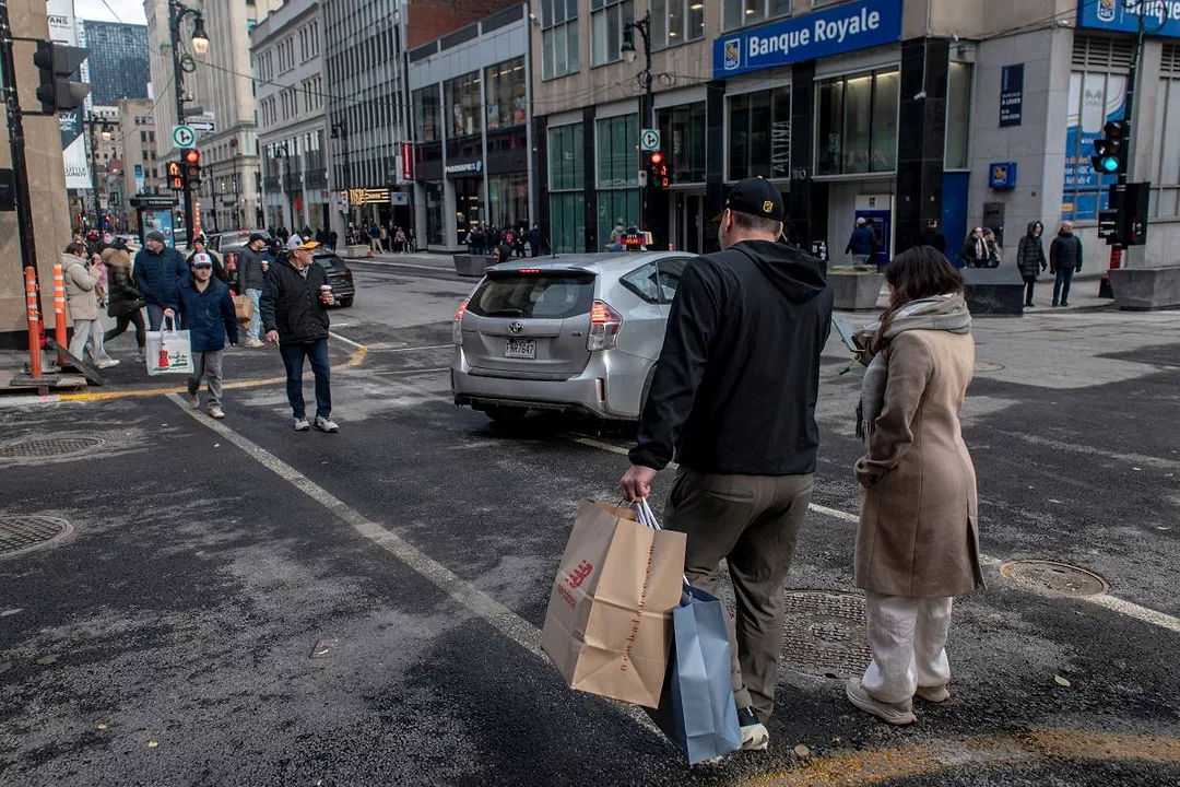 SHOPPERS CROSS A BUSY STREET IN A CITY, CARRYING SHOPPING BAGS