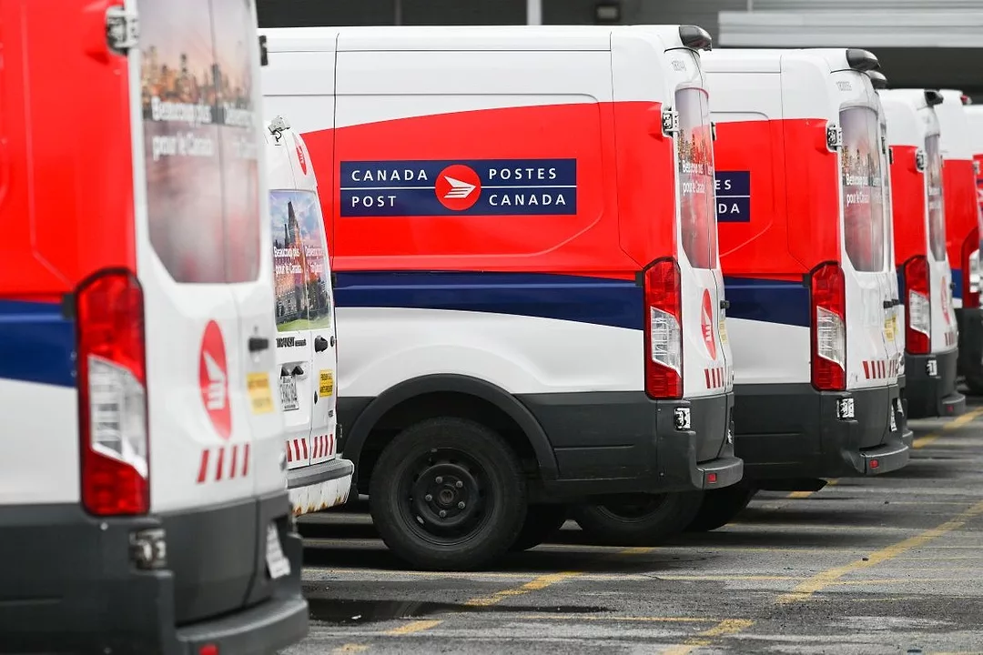 CANADA POST DELIVERY VANS SIT IN A ROW IN A PARKING LOT