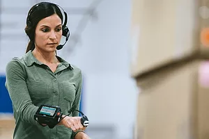 A WORKERS USES A WRIST-WORN DEVICE WITH A HEADSET IN A WAREHOUSE