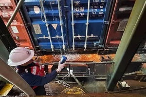 A WORKER IN A HARD HAT APPROACHES A STACK OF CONTAINERS LEAKING WATER