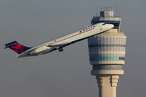 A DELTA AIRLINES PLANE TAKES OFF IN FRONT OF AN AIRPORT CONTROL TOWER
