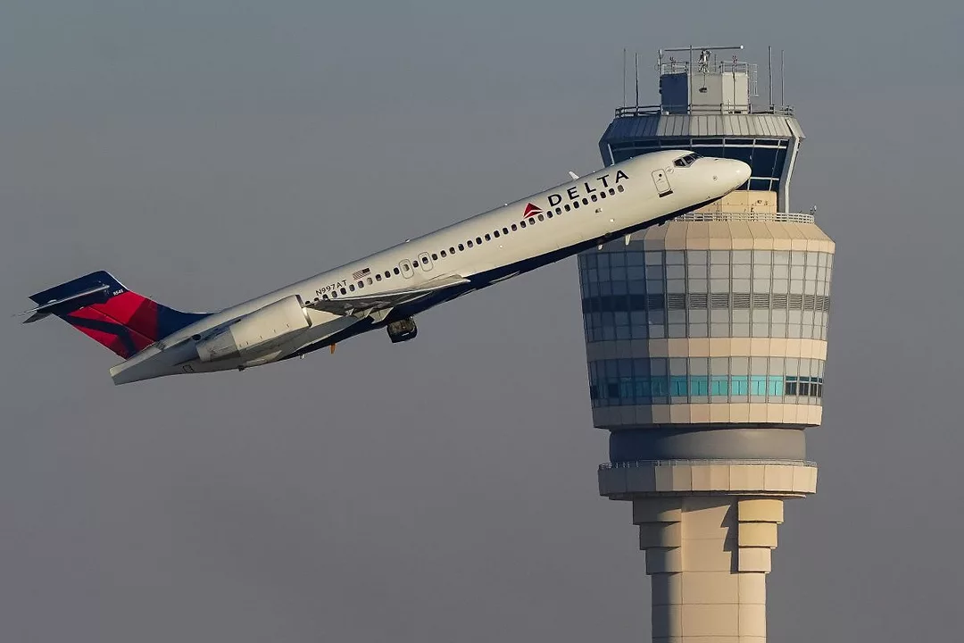 A DELTA AIRLINES PLANE TAKES OFF IN FRONT OF AN AIRPORT CONTROL TOWER