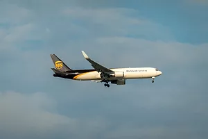 A white airplane with a brown tail and wings, flying through the air on a cloudy day