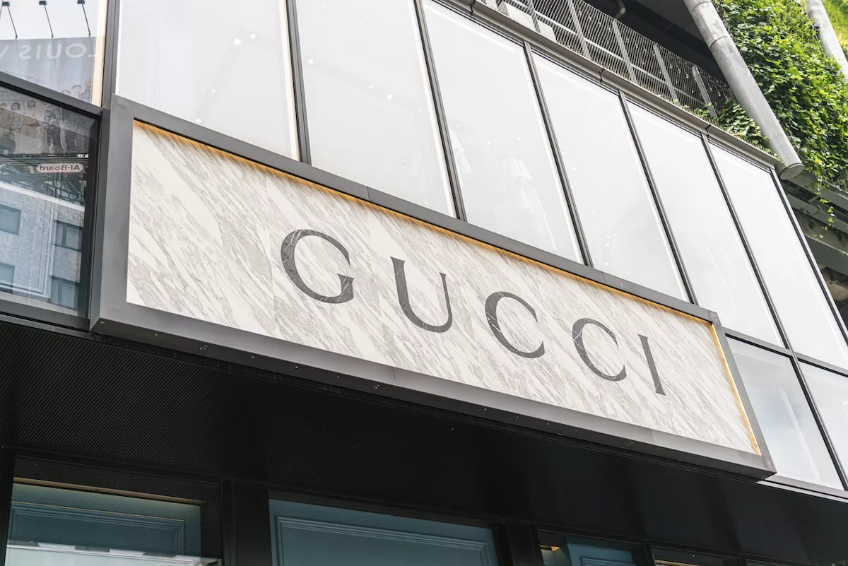 Bir mağazanın üzerinde, siyah çerçeveli beyaz tabelada büyük siyah harflerle GUCCI yazıyor