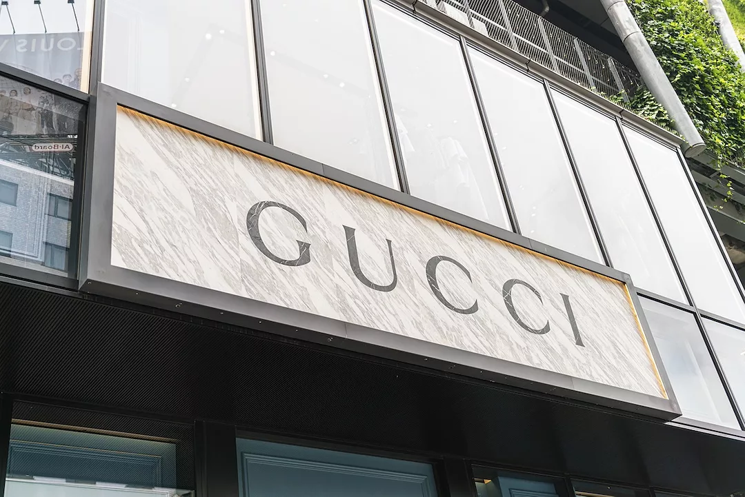 A white sign with a black border above a storefront, that reads "GUCCI" in large black lettering