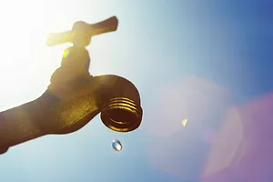 An outdoor brass water spigot on a bright sunny day, with a single drop of water coming out
