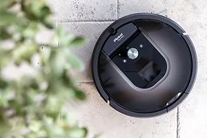 A black, circular robot vacuum on a white brick surface