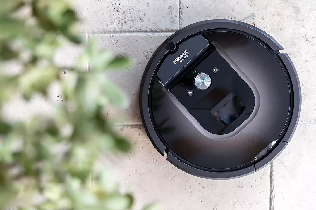 A black, circular robot vacuum on a white brick surface