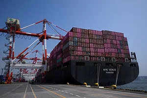 A CONTAINER SHIP STACKED HIGH WITH CONTAINERS SITS AT A DOCK WITH CRANES
