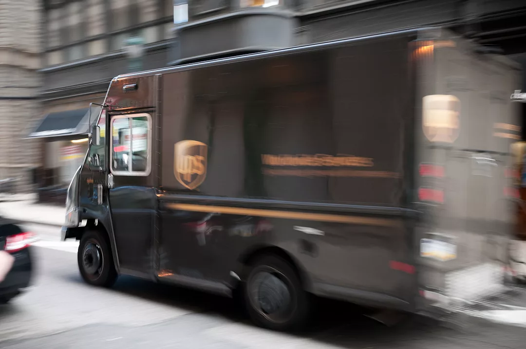 A BLURRY PHOTO OF A BROWN DELIVERY TRUCK ON AN URBAN STREET