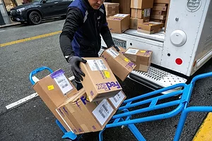 A WORKER WEARING GLOVES MOVES PACKAGES FROM THE BACK OF A VAN ONTO A HANDTRUCK