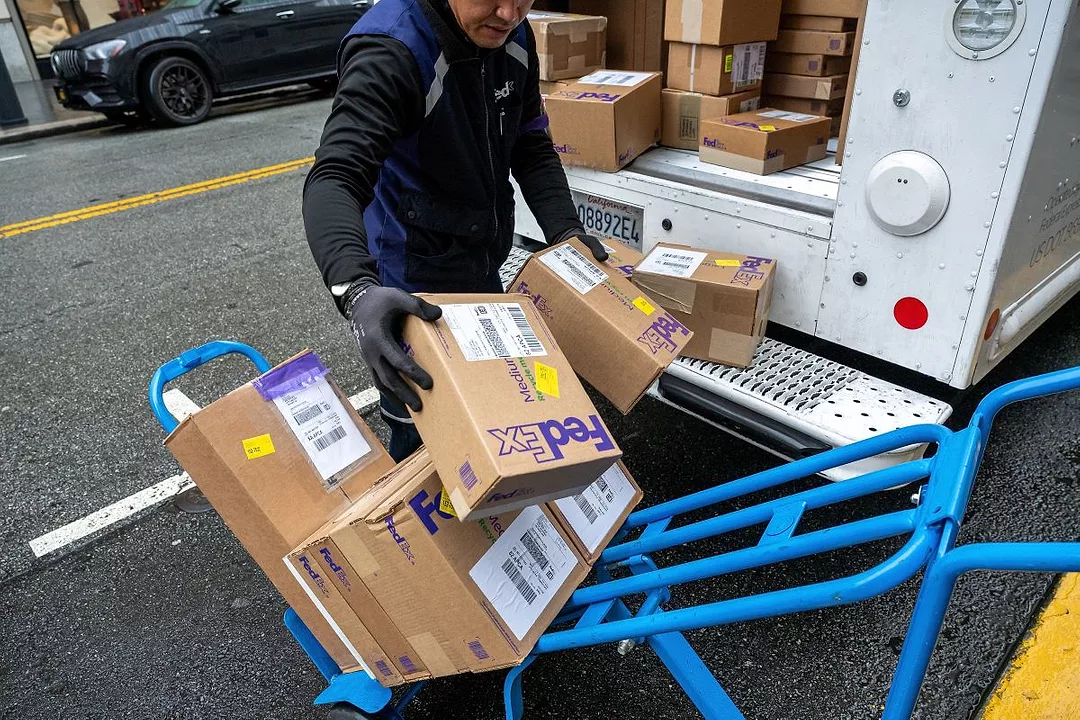 A WORKER WEARING GLOVES MOVES PACKAGES FROM THE BACK OF A VAN ONTO A HANDTRUCK