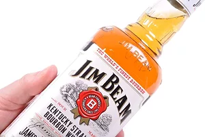 A HAND HOLDS UP A BOTTLE OF JIM BEAM WHISKEY TO THE LIGHT