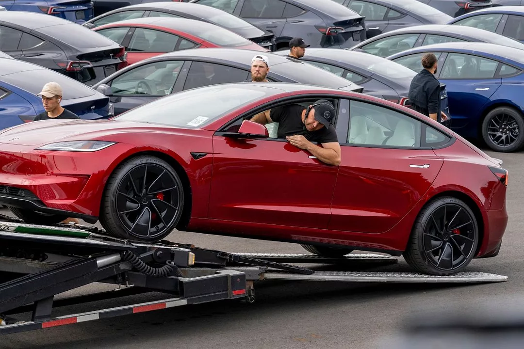 A DRIVER GUIDES A RED CAR ONTO A LIFT TRUCK BED