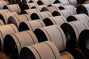 MULTIPLE BROWN COILS OF STEEL LIE ON A FACTORY FLOOR