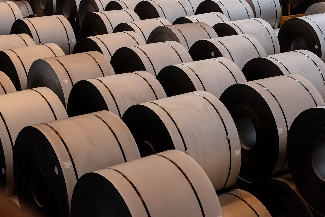 MULTIPLE BROWN COILS OF STEEL LIE ON A FACTORY FLOOR