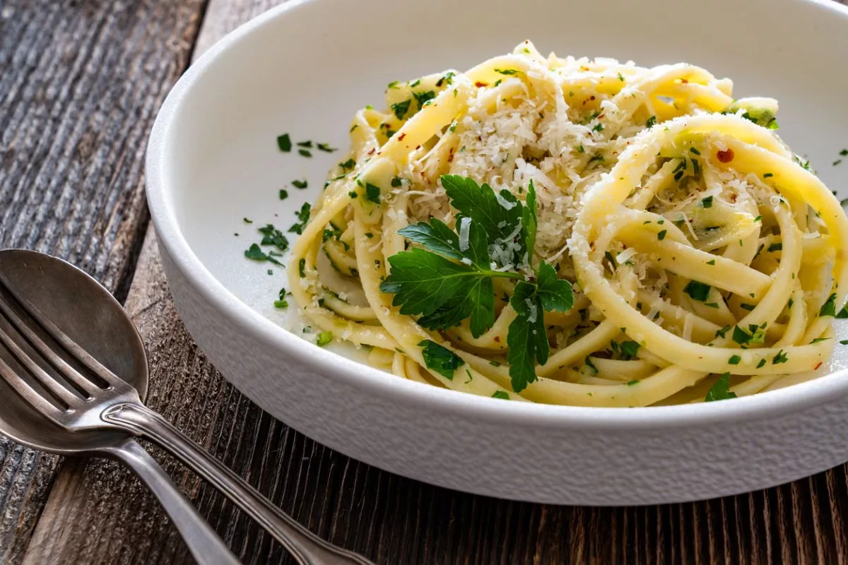 Ahşap masa üzerinde zeytinyağı, parmesan ve sarımsakla hazırlanmış bir kase makarna